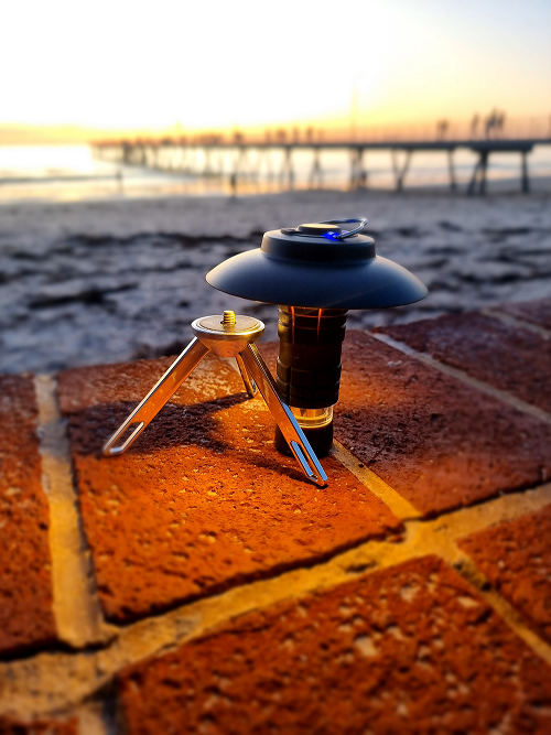 Background has a jetty with a sunset and the focus is the Multifunctional Lantern matching with its amber light on top of a red colour brick wall